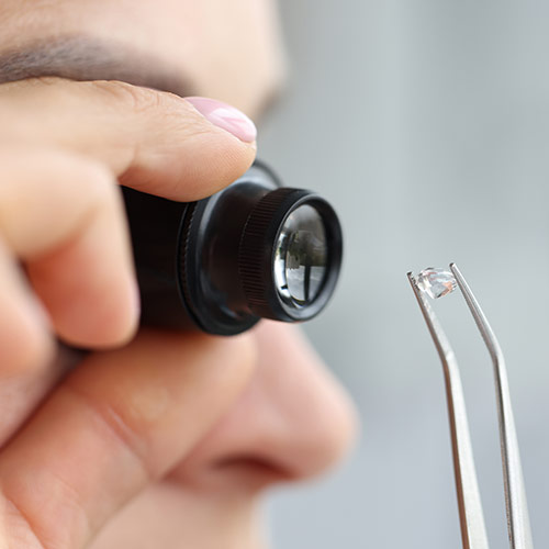 Frau betrachtet einen Diamanten mit einer Lupe und hält ihn mit einer Zange – Symbol für geprüfte Qualität und transparente Bewertung bei Diamanten als Sachwertanlage.