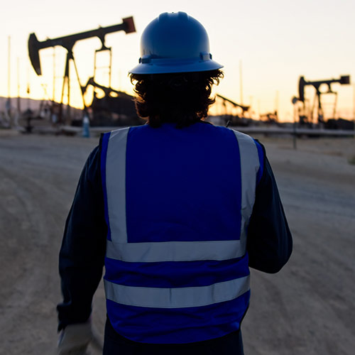 Arbeiter mit Schutzhelm auf einem US-Ölfeld bei Sonnenuntergang, im Hintergrund mehrere Ölpumpen – Symbol für reale Wertschöpfung und geprüfte Partner.